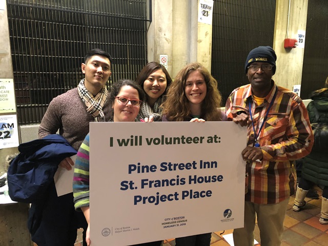 Five people hold a sign that says "I will volunteer at Pine Street Inn, St. Francis House, Project Place"